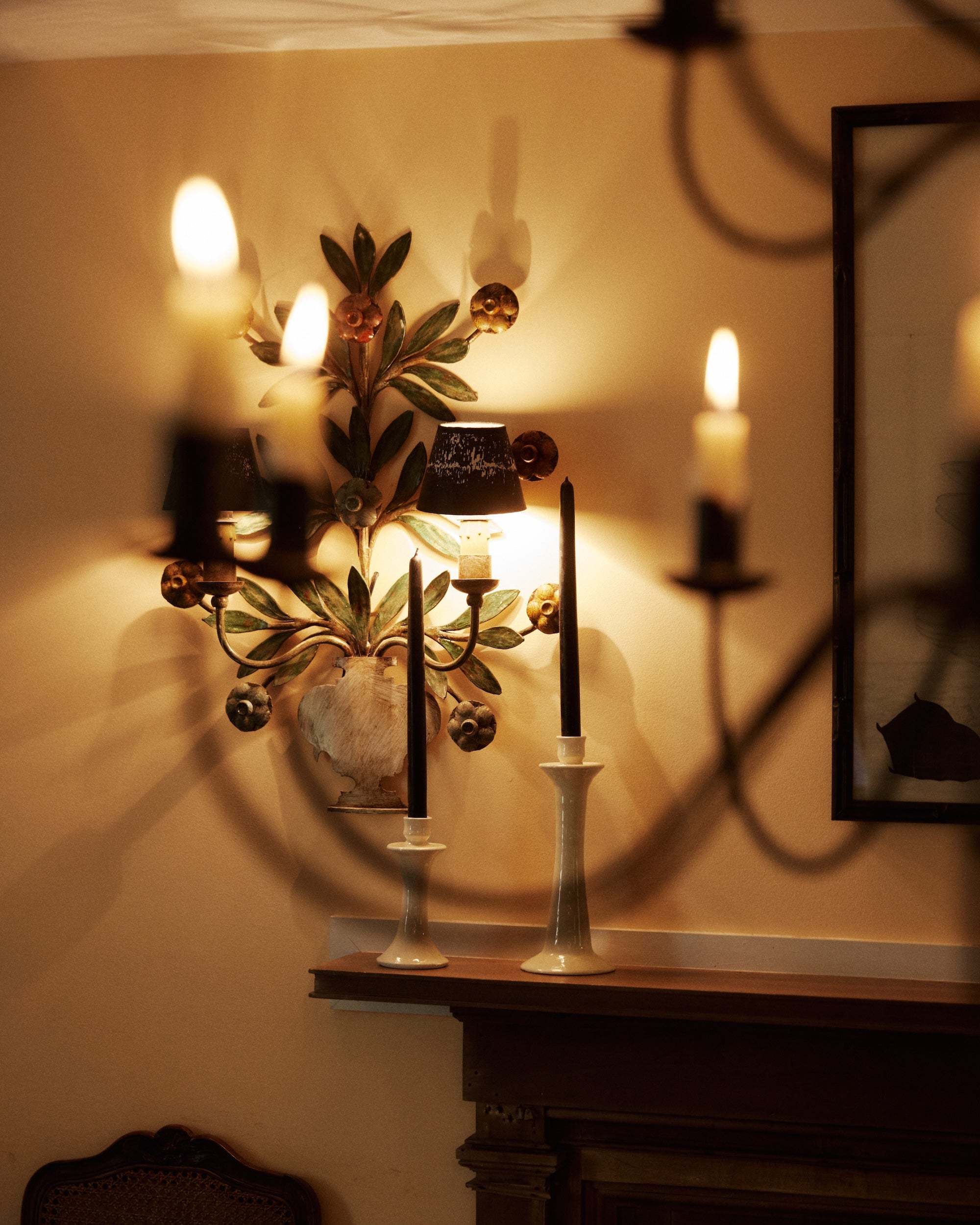 Two Tapered Candles, Set of 2 in white holders on a mantel, with glowing wall sconces adding warm light to a softly decorated room.