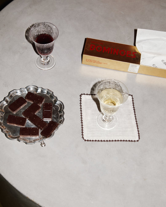 Two glasses of wine, a plate of chocolate bars, and a box of Dominoes on a gray surface.