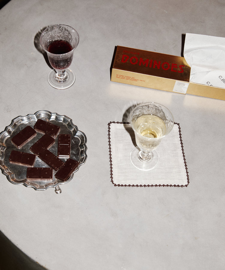 Two glasses of wine, a plate of chocolate bars, and a box of Dominoes on a gray surface.