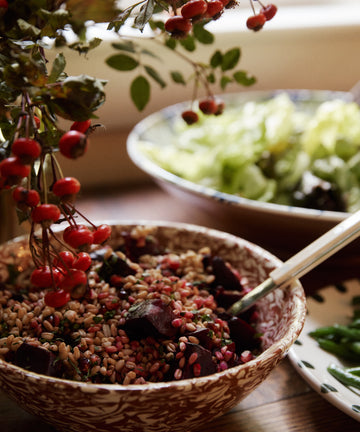 A grain and beet salad fills the Celine Salad Bowl, placed on a table beside leafy greens and red berries.