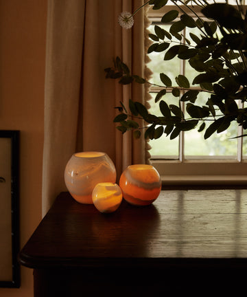 Three lit candles in Akila Candleholder handcrafted from Egyptian Alabaster sit on a dark table, filling the room with warm light and unique stone decor charm.