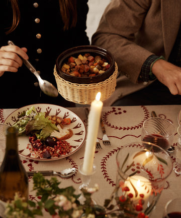 Two people sit at a candlelit table set with the Vito Dinner Plate, Set of 4, enjoying drinks and roasted vegetables as they prepare to serve themselves.