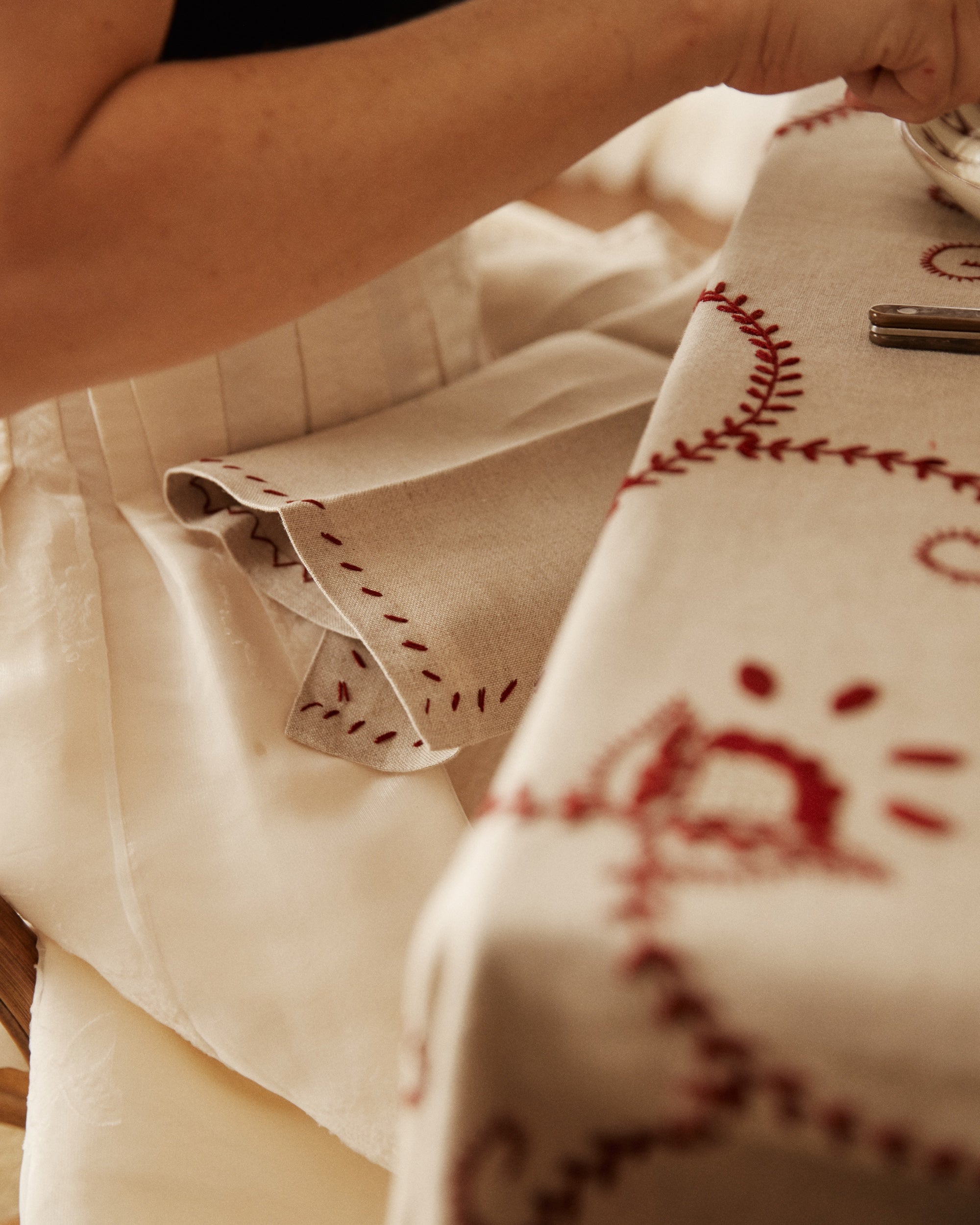 A person rests their arm on a table set with a raw linen tablecloth and the Inez Napkin, Set of 6, holding a plate; only their arm and torso are shown.