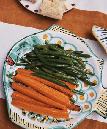 Steamed green beans and carrot sticks are arranged on the Rico Serving Platter, a charming fish-shaped dish, with bread visible in the background.