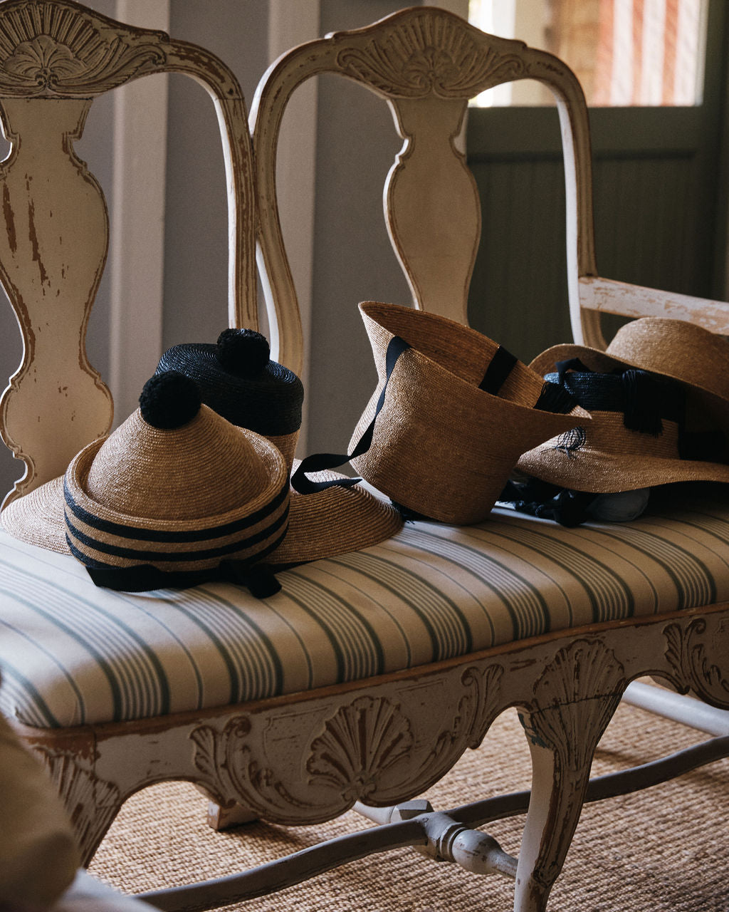 Two Circus Hats and two straw berets with black bands, pom-poms, and long black ties are placed on a vintage upholstered bench featuring intricate wooden details.