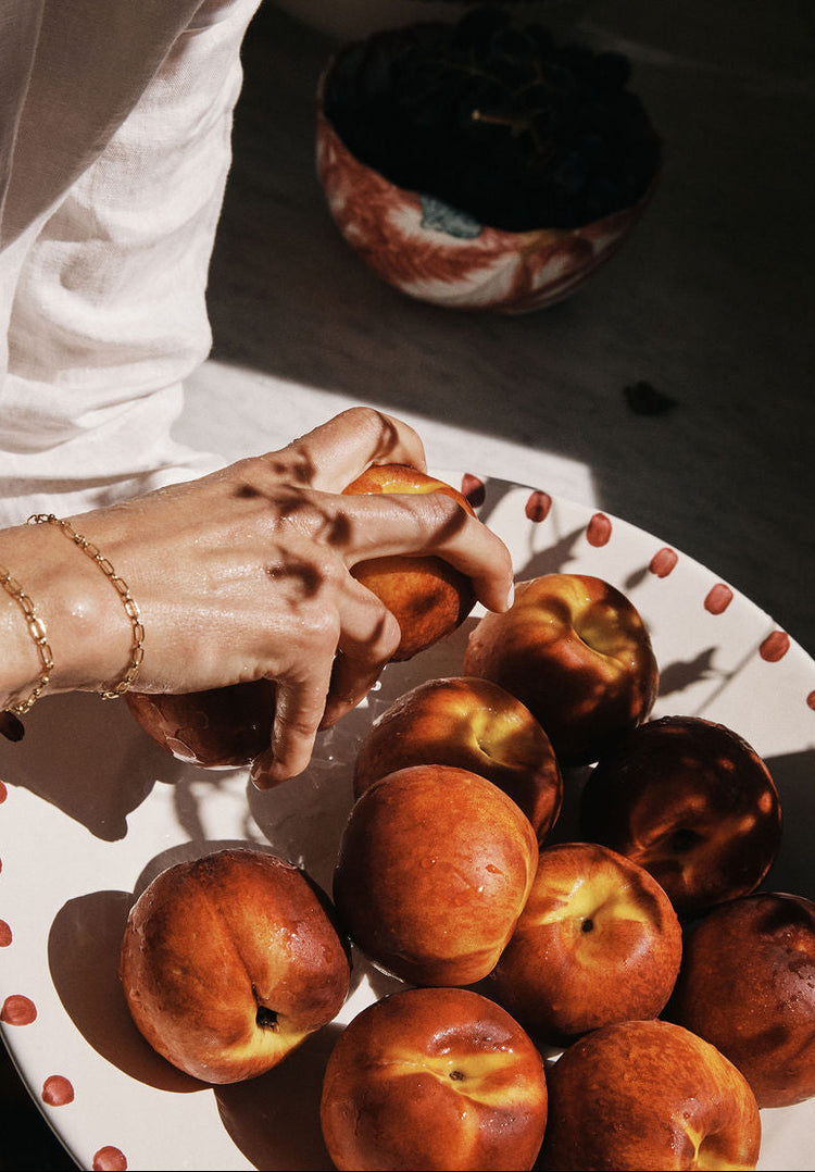 Person holding a peach over a plate of peaches with a dark background