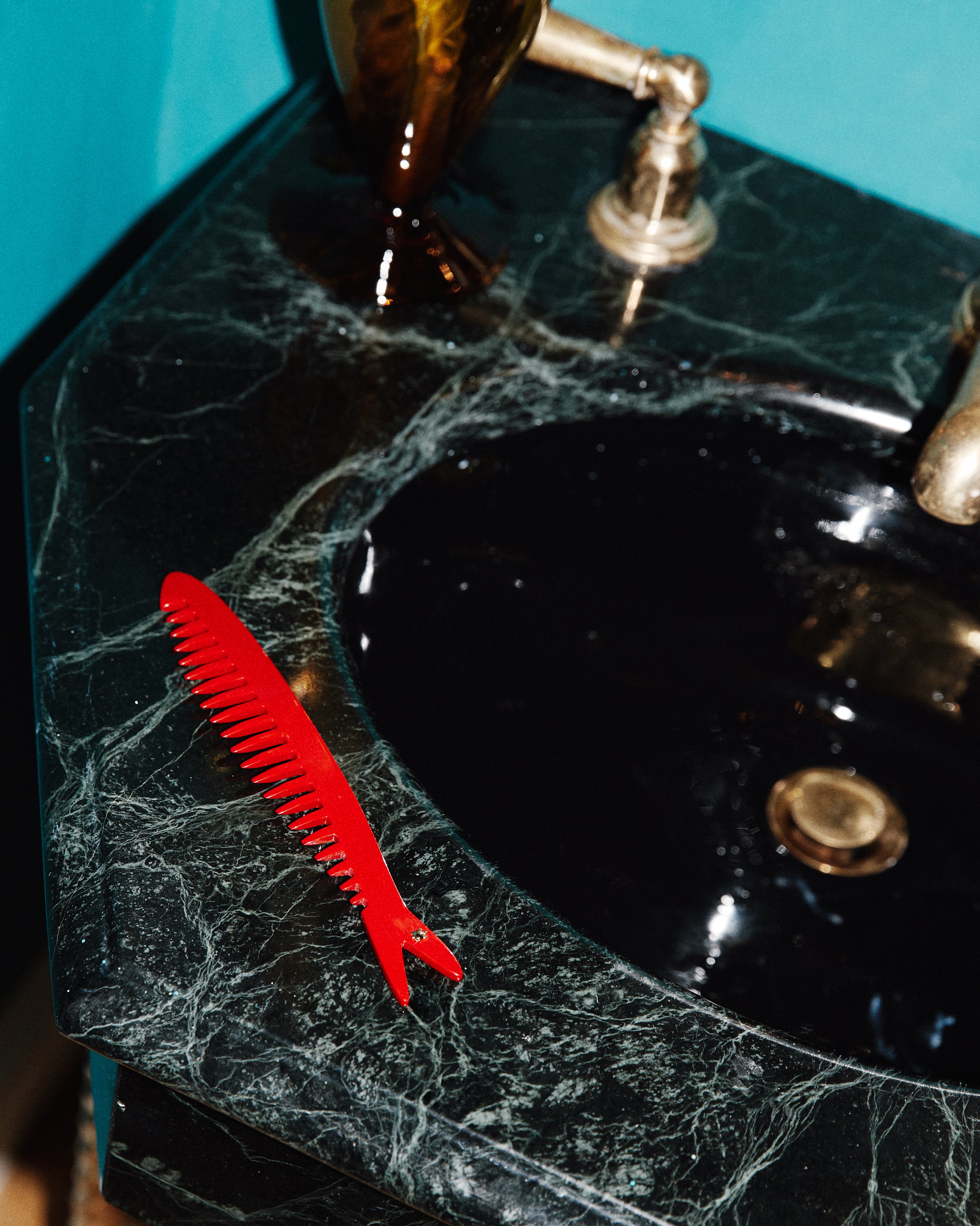A Capri Sardine Comb rests on a dark green marble bathroom sink next to a brass faucet.