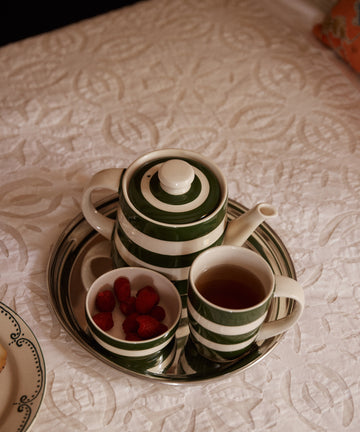 A kitchen staple: the Classic Teapot, a cup of tea, and fresh raspberries sit on a silver tray over a white textured tablecloth.