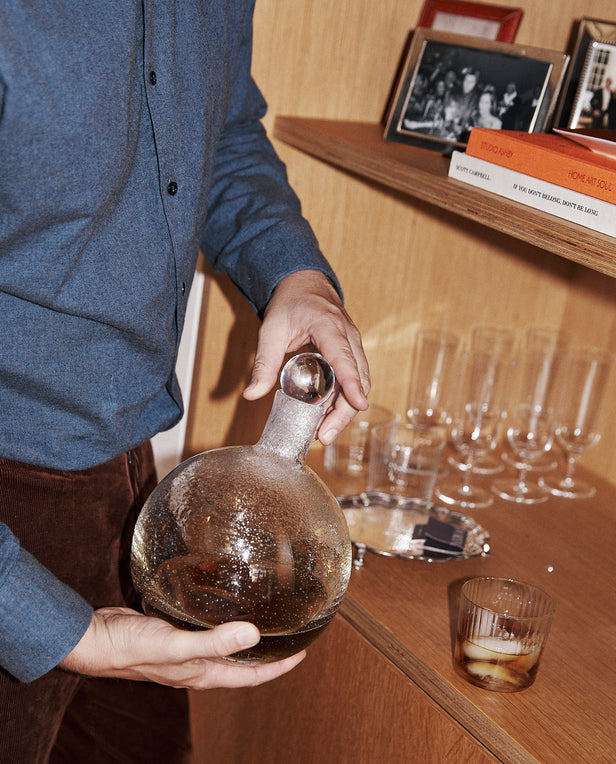 Person holding a glass decanter with a wooden shelf in the background