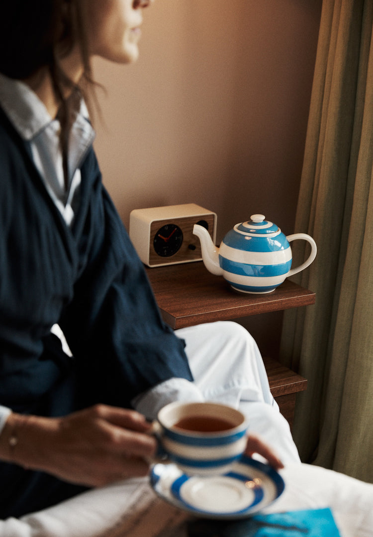 Person holding a striped teacup and saucer with a striped teapot in the background.