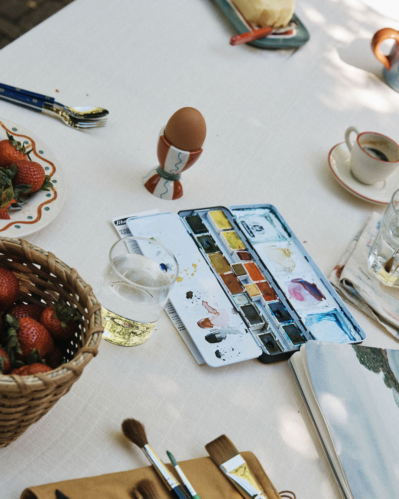 Artistic setup with watercolor set, brushes, and snacks on a table.