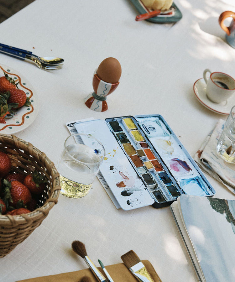 Artistic setup with watercolor set, brushes, and snacks on a table.