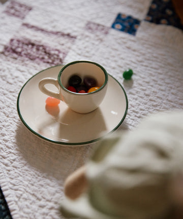 The Gio Espresso Set holds vibrant jellybeans on its saucer atop a white quilted surface, with extra jellybeans scattered nearby.