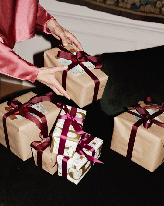 Person exchanging wrapped gifts with red ribbons on a dark surface