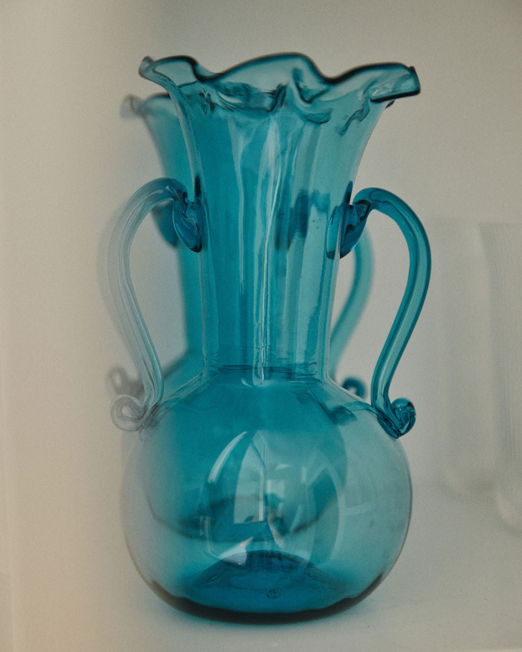 The Camilla Vase is a translucent blue, hand-blown glass vase with two handles and a fluted rim—perfect for adding a unique touch to your decorative vases collection.