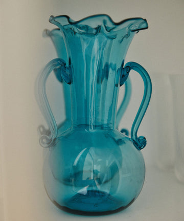 The Camilla Vase is a translucent blue, hand-blown glass vase with two handles and a fluted rim—perfect for adding a unique touch to your decorative vases collection.