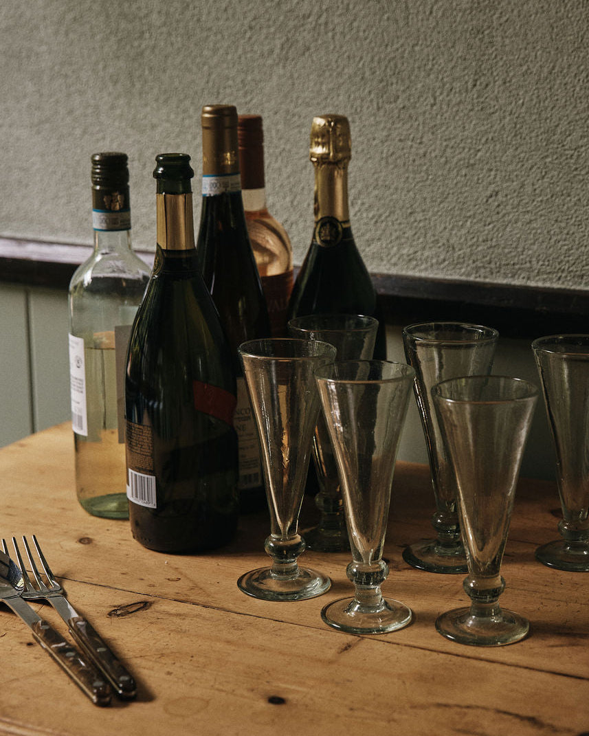 A set of six Elodie Champagne Glasses is arranged on a wooden table with several empty wine and champagne bottles, two forks, and two knives.