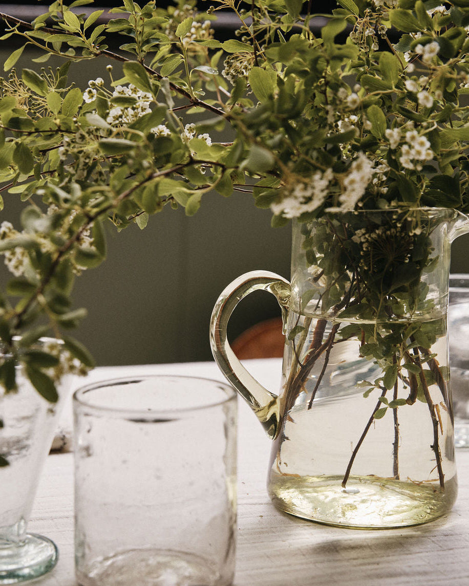 Clear glass pitcher with greenery on a table