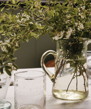 Clear glass pitcher with greenery on a table