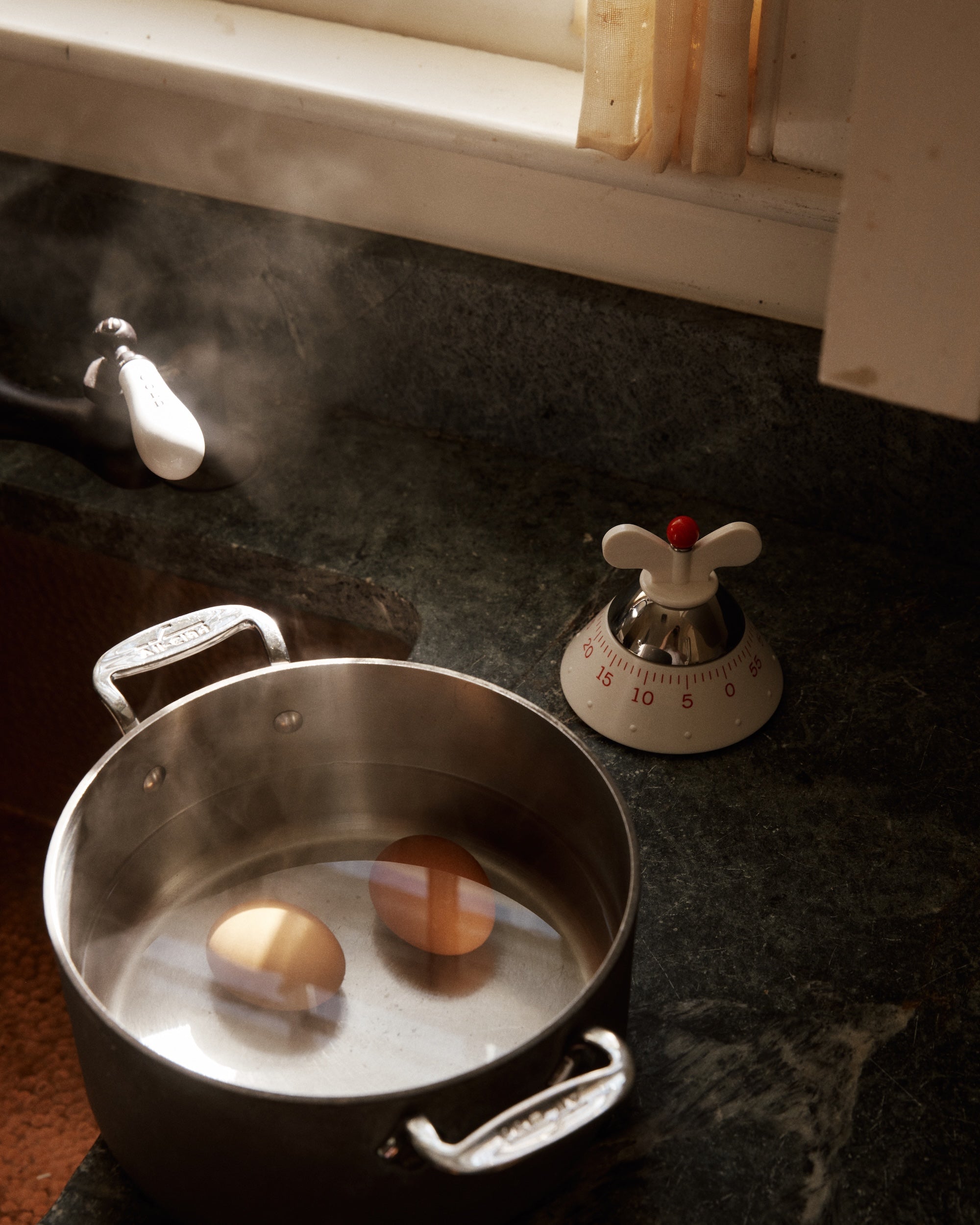 Two eggs boil in a pot with steam rising, while the Kitchen Timer sits nearby on the dark countertop, perfectly tracking the cooking time.
