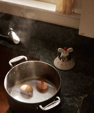 Two eggs boil in a pot with steam rising, while the Kitchen Timer sits nearby on the dark countertop, perfectly tracking the cooking time.