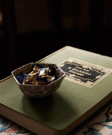 The Celine Snack Bowl filled with wrapped candies sits on a closed green book titled Changing Ireland atop a floral-patterned surface.