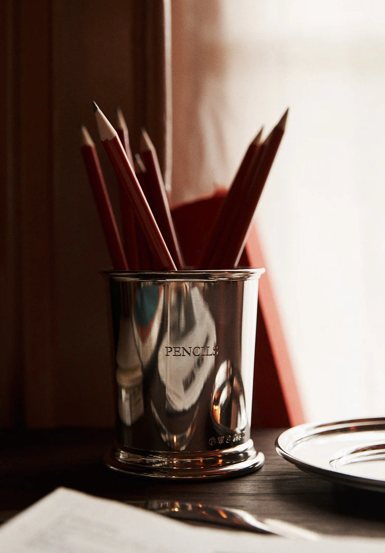 Silver pencil holder with red pencils on a wooden surface