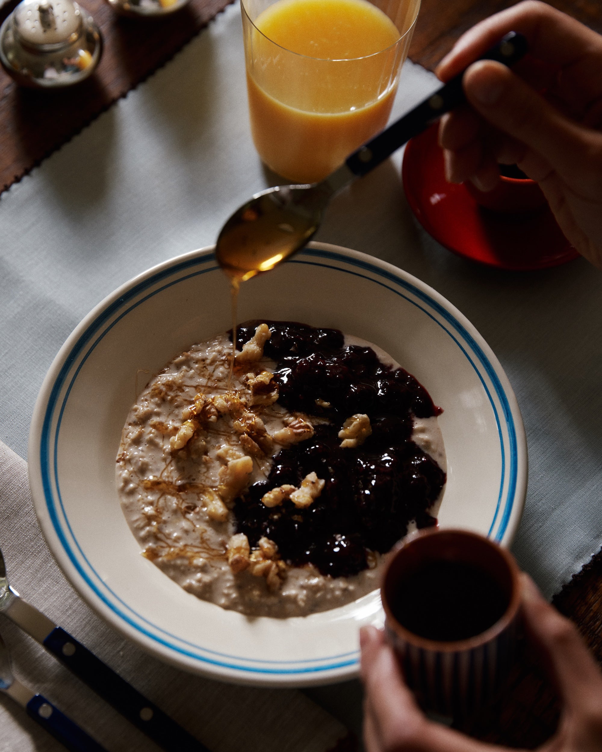 A bowl of oatmeal in the Folk Pasta Bowl, Jester, topped with walnuts and fruit compote, honey drizzle, orange juice, and mix-and-match tableware on the table.