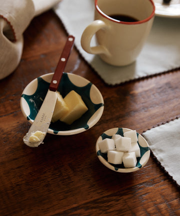 A table with a coffee cup, butter dish and knife, sugar cubes in Stella Nesting Bowls, all on patterned plates.