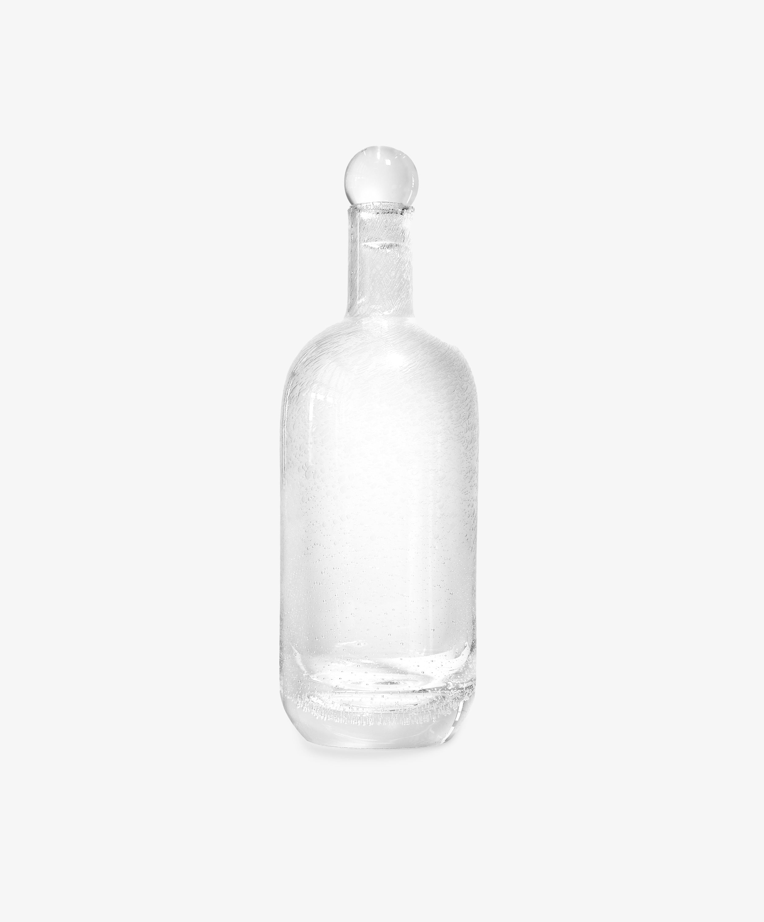 The Bubble Glass Carafe, crafted from clear hand-blown glass and topped with a round stopper, is showcased against a plain white background.