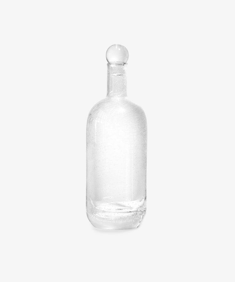 The Bubble Glass Carafe, crafted from clear hand-blown glass and topped with a round stopper, is showcased against a plain white background.