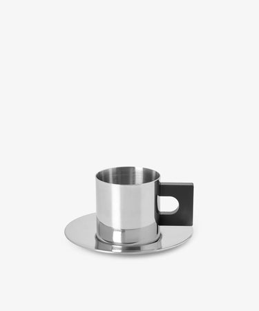 The S.R. Metal Cup & Saucer showcases Bauhaus style with a stainless steel body and black rectangular handle, paired with a matching saucer, set against a plain white background.