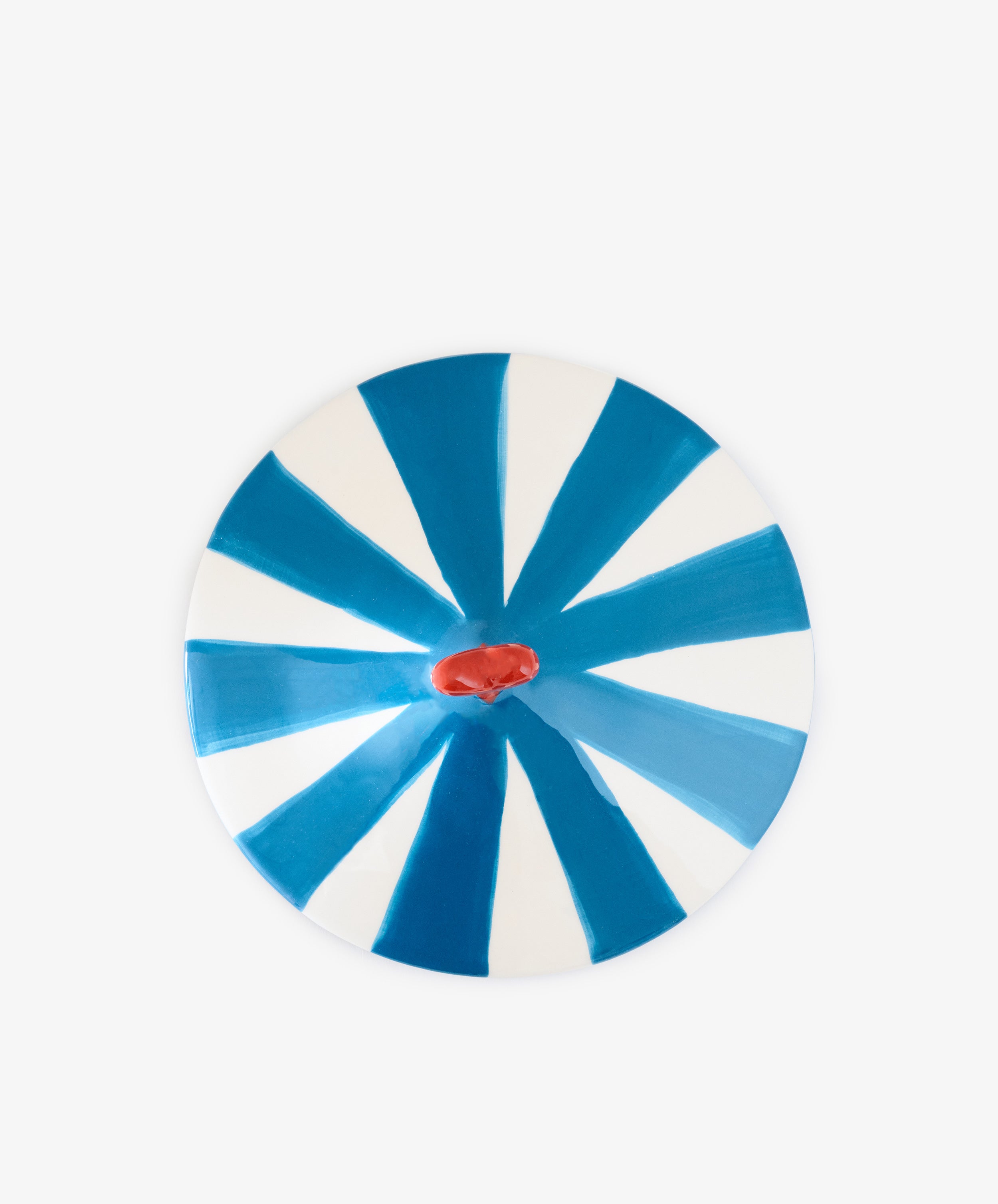 The Love Box, a round ceramic plate featuring alternating blue and white wedge-shaped stripes and a small red irregular shape in the center reminiscent of a circus tent box, makes for a delightful decorative accent.