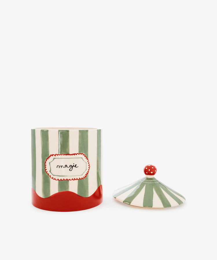 The Magic Box is a ceramic jar featuring green and white stripes reminiscent of a circus tent, with a red base and a label that reads 
