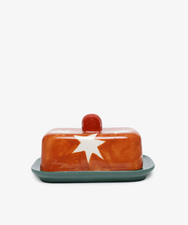 Butterfingers Butter Dish by Laetitia Rouget. Orange stoneware top with white starburst and green dish.