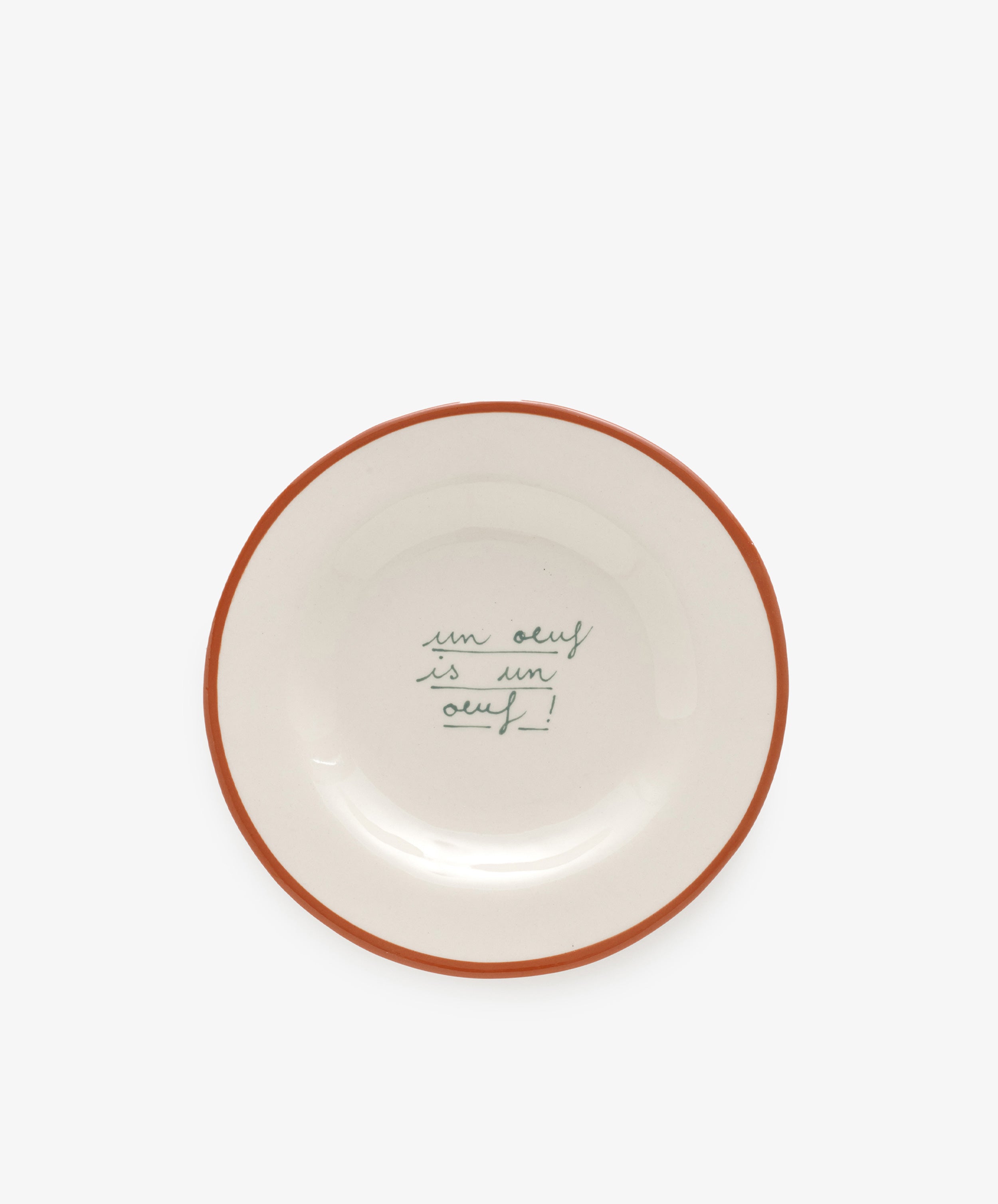 The Un oeuf is un oeuf plate is crafted from ceramic stoneware and features a brown rim with the phrase handwritten in green cursive at the center, reflecting Laetitia Rougets playful hand-painted style.