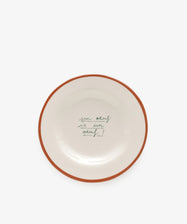 The Un oeuf is un oeuf plate is crafted from ceramic stoneware and features a brown rim with the phrase handwritten in green cursive at the center, reflecting Laetitia Rougets playful hand-painted style.
