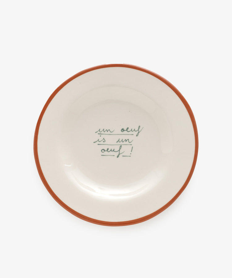 Un Oeuf is un Oeuf by Laetitia Rouget. White stoneware plate with red painted rim and cursive writing.