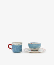 The Colombe Bundle features a blue mug with a red handle and white line art beside a blue bowl adorned with white stars on a matching saucer with a wavy red rim, all set against a white background.