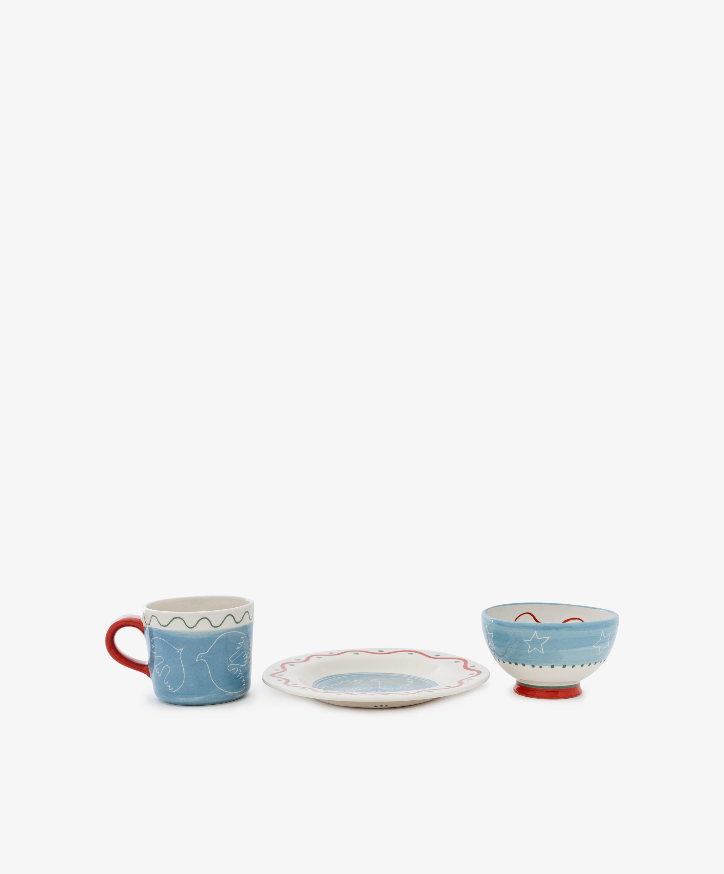 The Colombe Bundle, featuring a blue mug, plate, and blue bowl with red accents and abstract designs, is arranged in a row against a white background.
