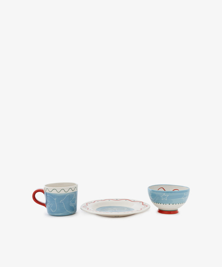 The Colombe Bundle, featuring a blue mug, plate, and blue bowl with red accents and abstract designs, is arranged in a row against a white background.