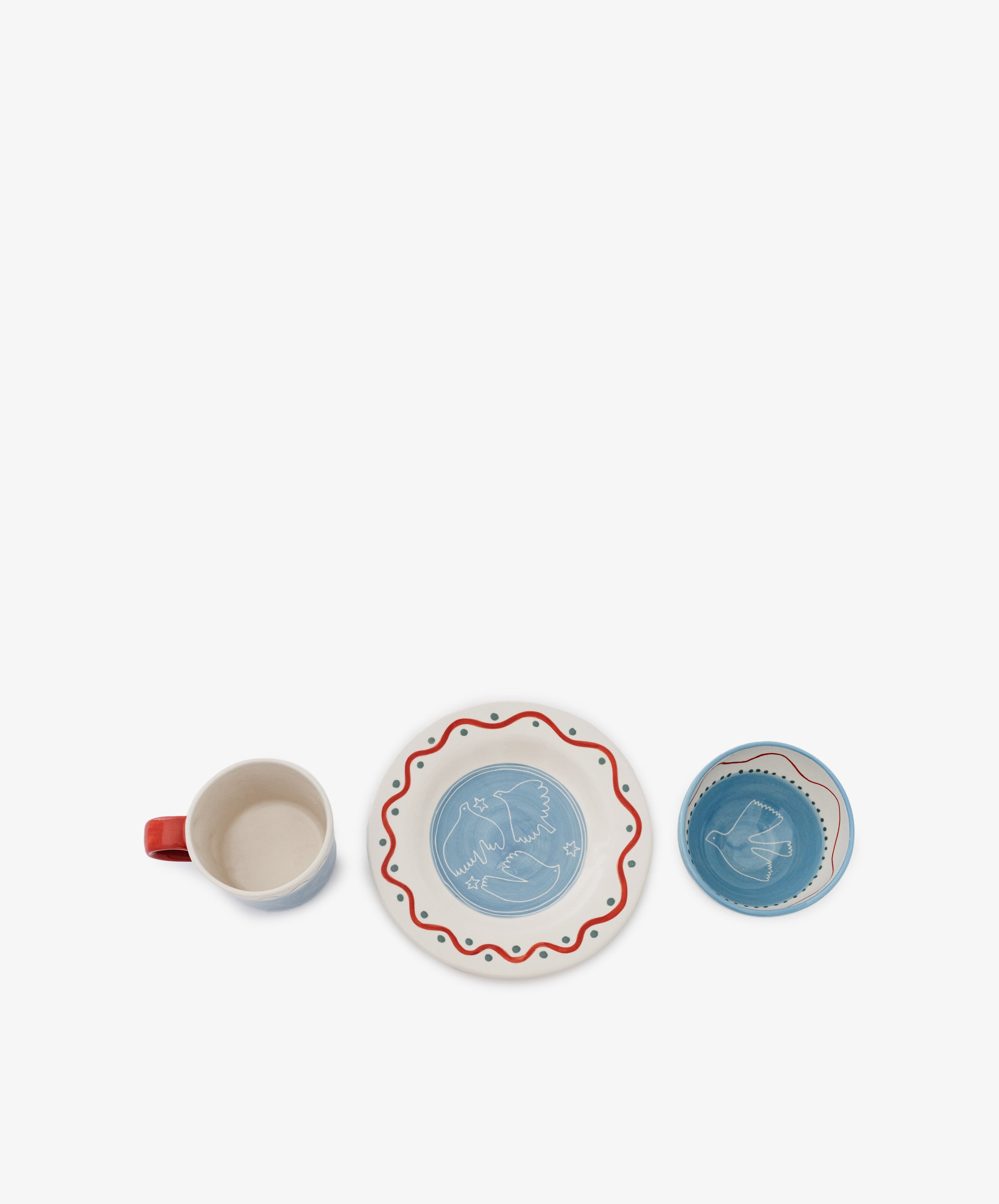 The Colombe Bundle features a ceramic mug, a plate with a red wavy border and bird motif, and a matching blue bowl, all arranged in a row on a white background.