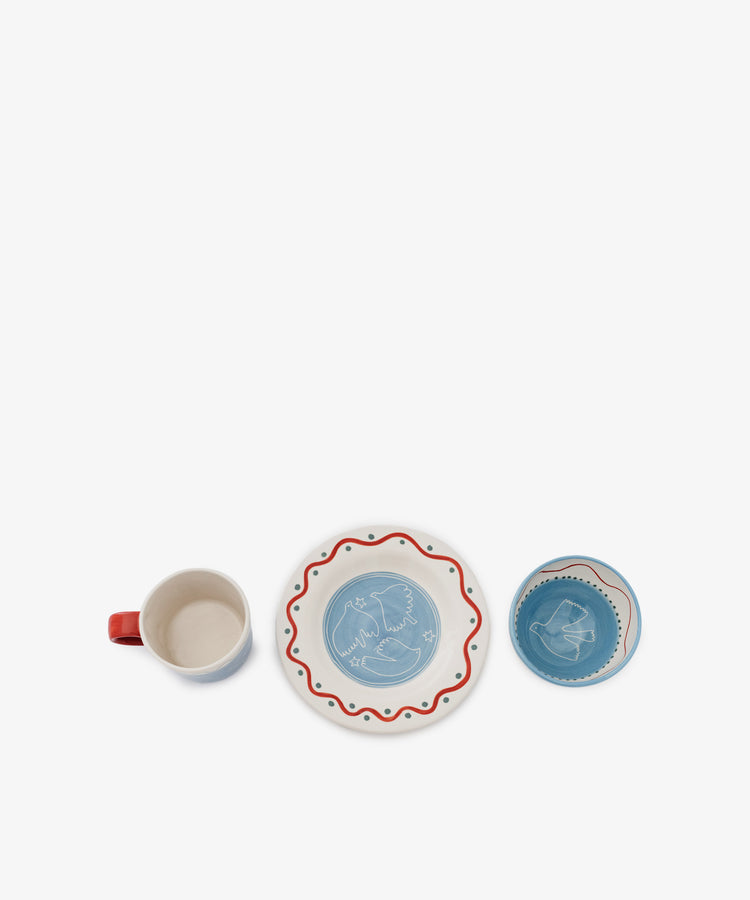 The Colombe Bundle features a ceramic mug, a plate with a red wavy border and bird motif, and a matching blue bowl, all arranged in a row on a white background.