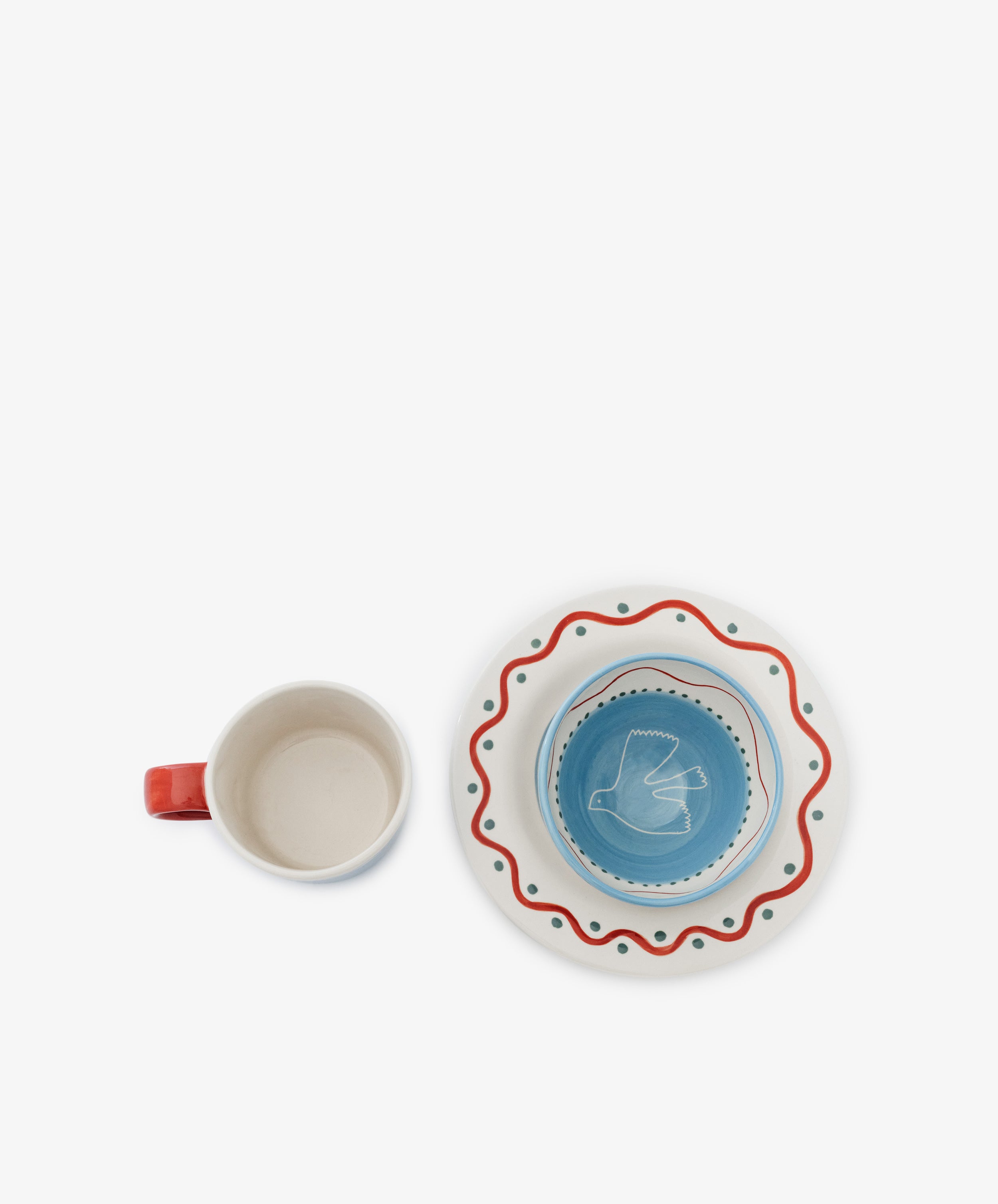 The Colombe Bundle features a white mug with a red handle beside a blue bowl stacked on a white plate decorated with red wavy and green dotted patterns.