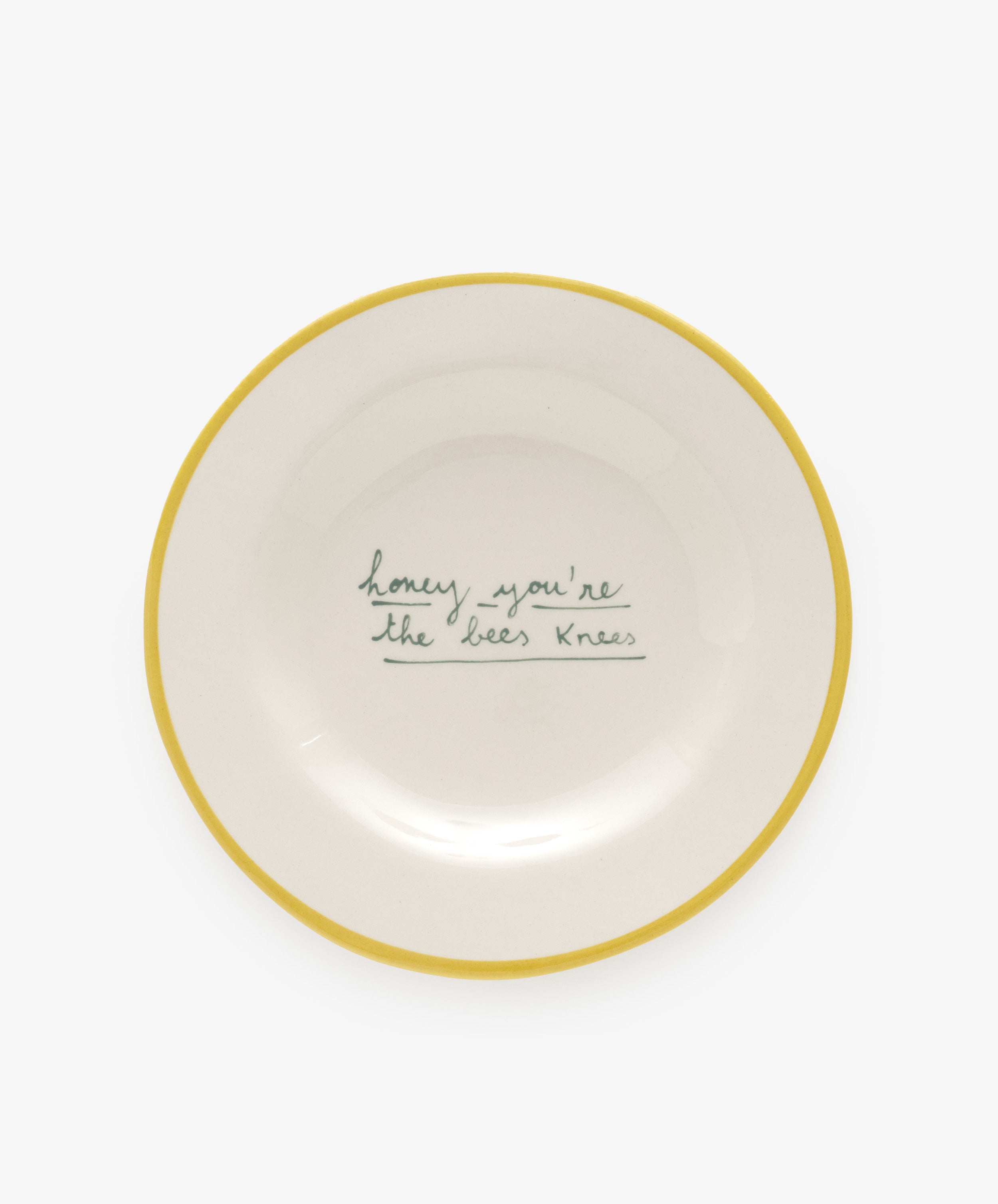 Honey, you're the bees knees by Laetitia Rouget. White stoneware plate with yellow stripe border and cursive text.