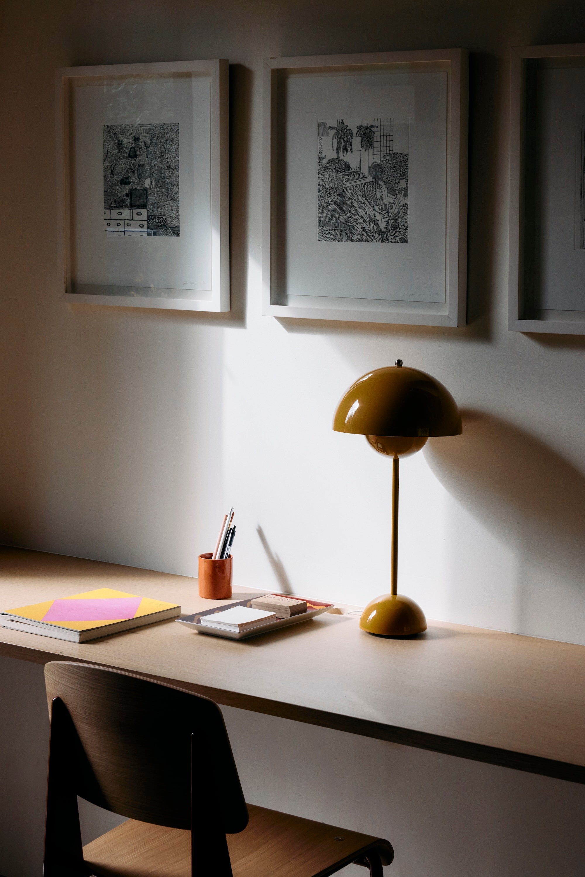A minimalist desk with a yellow lamp, unique presents, and the Dreamer's Notebook sits beneath three framed black-and-white artworks on the wall.