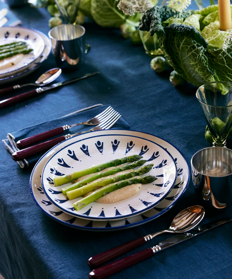 The Vito Dinner Plate, Set of 4, is shown on a set dining table topped with cooked asparagus spears, elegant dinnerware, silverware, cups, and green leafy centerpieces.