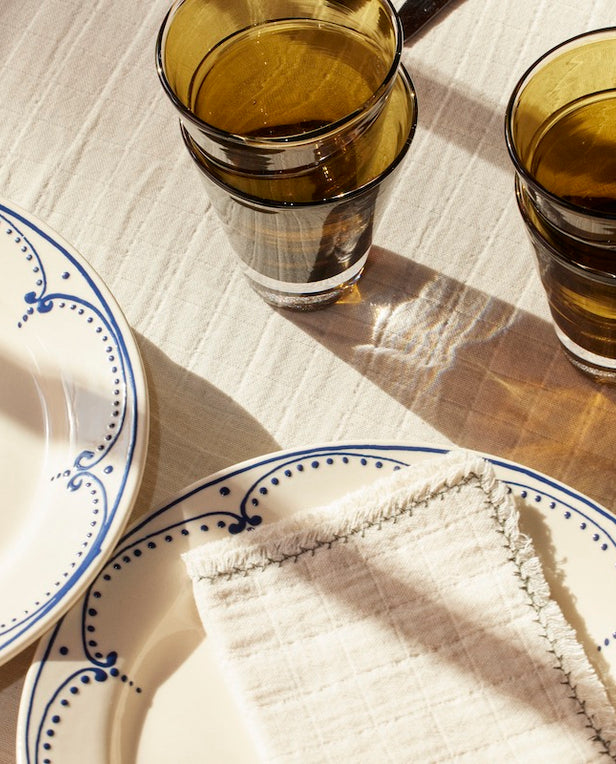 linen napkins on cream plates with green glasses stacked on top of linen table