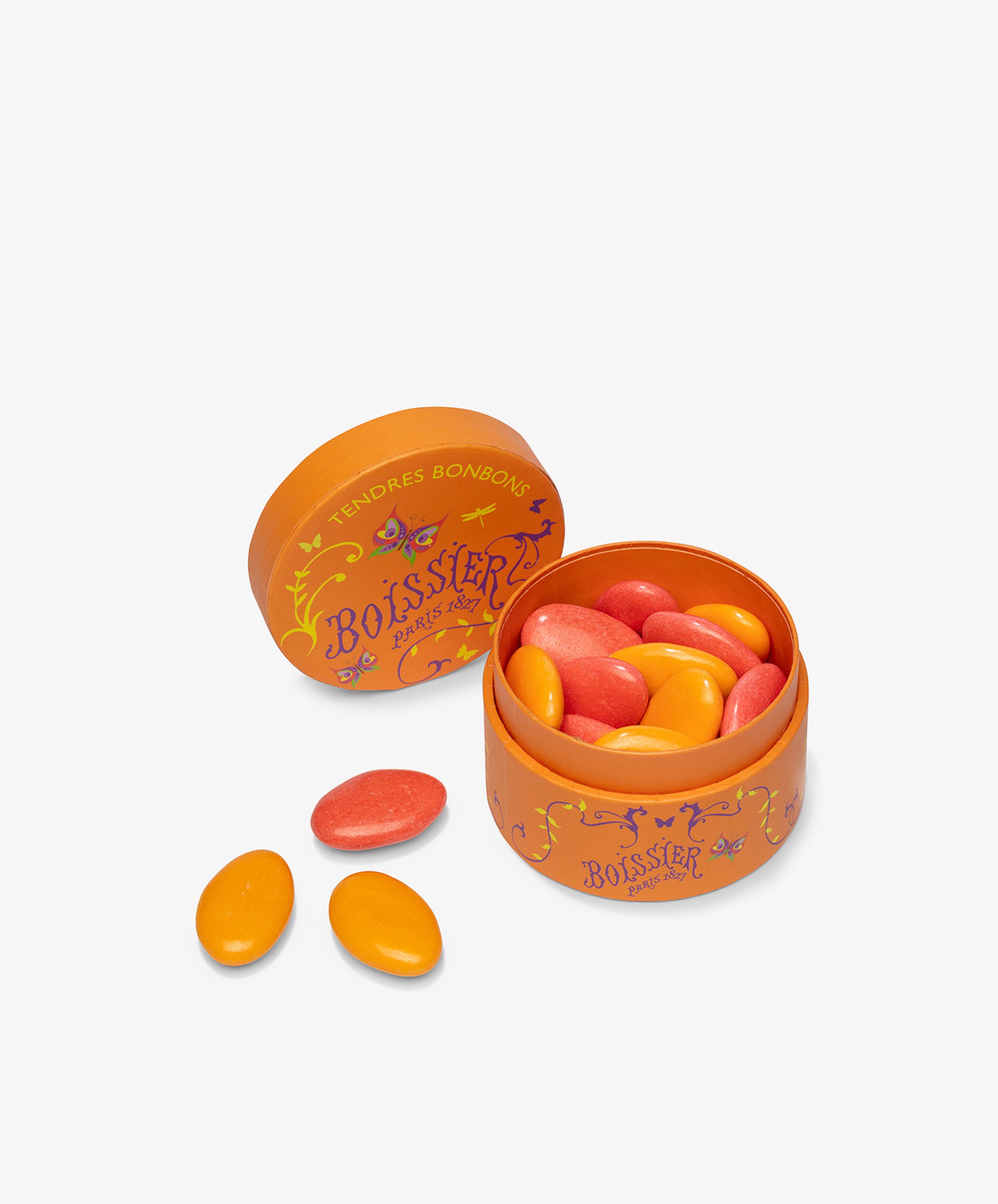 An open round orange tin of Multicolored Chocolate Gems with pink and orange candies inside, crafted by Maison Boissier, and three candies placed beside the tin on a white background.