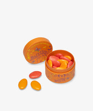 An open round orange tin of Multicolored Chocolate Gems with pink and orange candies inside, crafted by Maison Boissier, and three candies placed beside the tin on a white background.